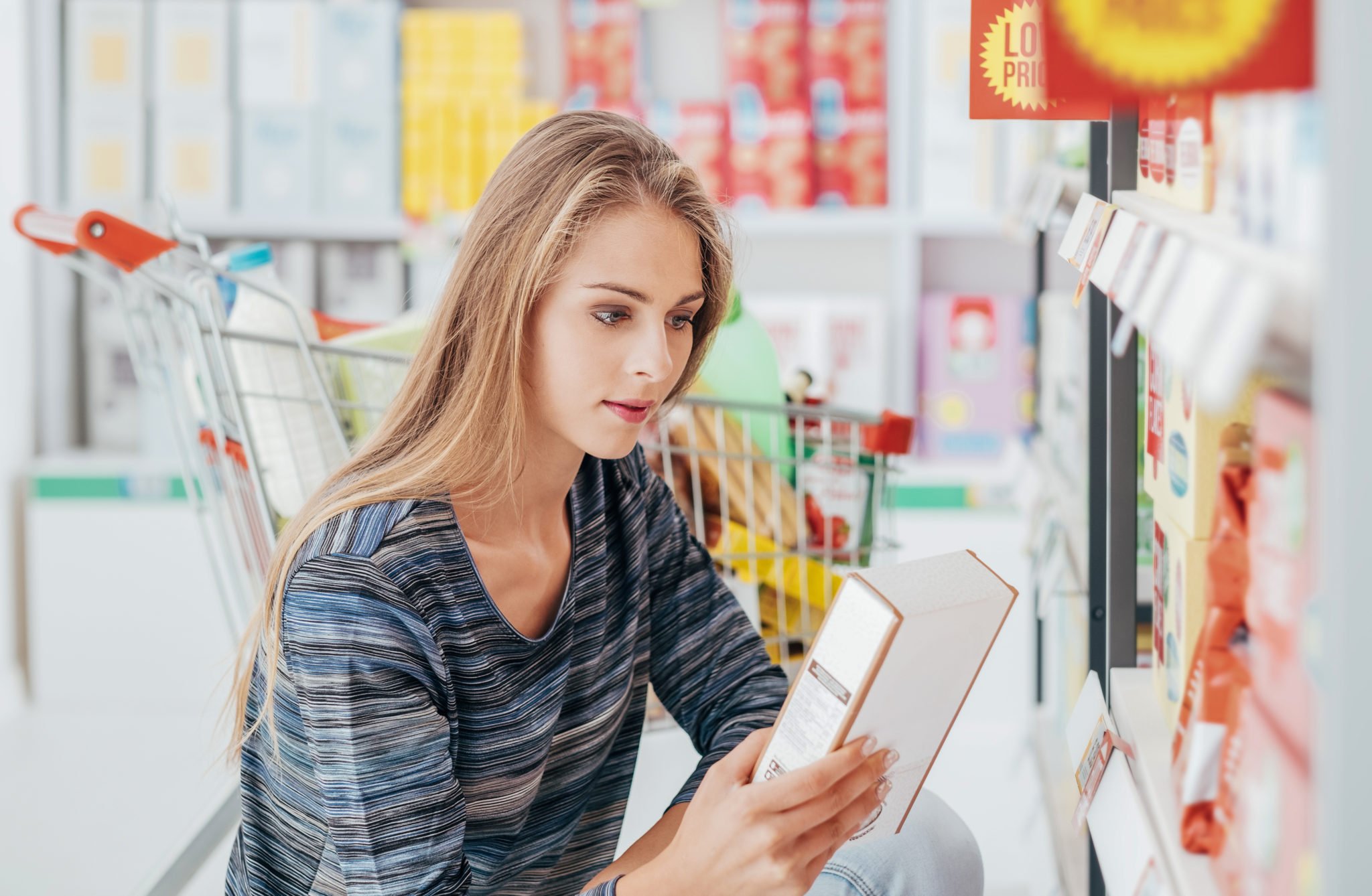 Young woman doing grocery shopping at the supermarket and reading a food label with ingredients on a box, using Nutrigenomics to inform health choices